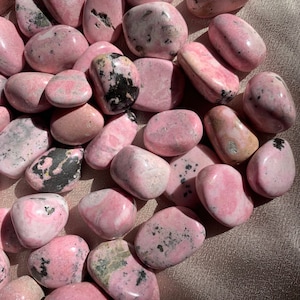 May include: A collection of pink and black tumbled stones. The stones are smooth and polished, with a variety of shapes and sizes.