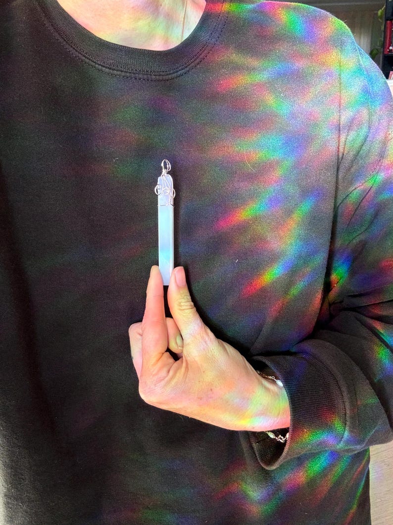 Pu&ograve; includere: Un ciondolo di cristallo bianco con una catena d'argento e una parte superiore decorativa. Il ciondolo &egrave; tenuto da una mano.