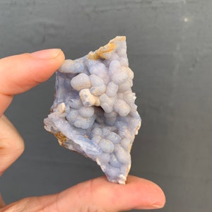 May include: A blue and white agate geode with a cluster of small, round, blue crystals. The geode is about the size of a person's hand.