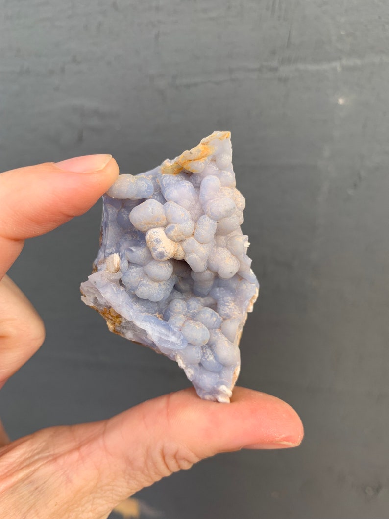 May include: A blue and white agate geode with a cluster of small, round, blue crystals. The geode is about the size of a person's hand.
