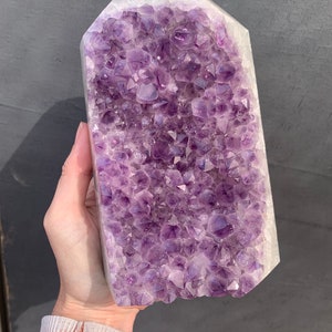 May include: A large amethyst crystal cluster with a natural, raw exterior and a smooth, polished base. The crystal is a deep purple colour and has a variety of sizes and shapes of points.