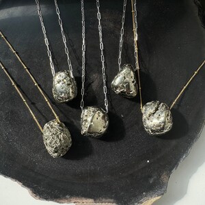 May include: Six silver necklaces with different sized and shaped pyrite stones hanging from them on a black surface.