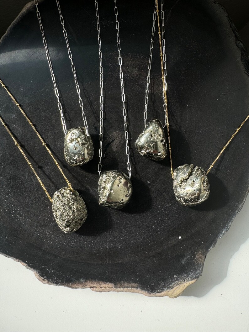 May include: Six silver necklaces with different sized and shaped pyrite stones hanging from them on a black surface.