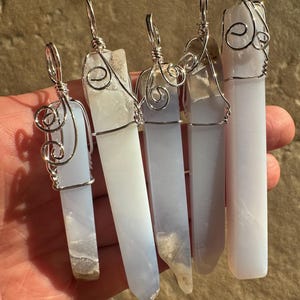 Pu&ograve; includere: Cinque ciondoli in cristallo di agata blu avvolti in filo d'argento. Ogni ciondolo &egrave; di dimensioni e forma diverse. I ciondoli sono tutti appesi a una catena d'argento.