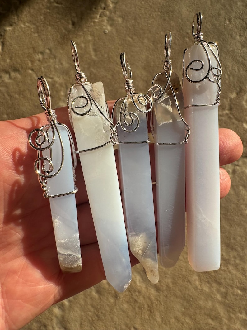 Pu&ograve; includere: Cinque ciondoli in cristallo di agata blu avvolti in filo d'argento. Ogni ciondolo &egrave; di dimensioni e forma diverse. I ciondoli sono tutti appesi a una catena d'argento.