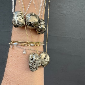 May include: A set of five gold necklaces with pyrite stone pendants. The necklaces are layered and feature different chain styles. The stones are a natural, rough, and textured gray color.