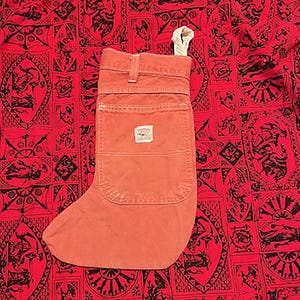May include: A bright orange stocking made from denim with a large front pocket. The stocking has a white tag on the pocket.