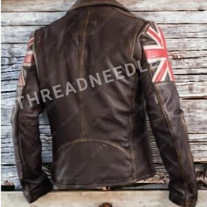 Puede incluir: Chaqueta de cuero marr&oacute;n con dise&ntilde;o de la bandera brit&aacute;nica en los hombros. La chaqueta tiene un cuello cl&aacute;sico y un acabado envejecido. El texto "THREADNEEDLE" es visible en la chaqueta.