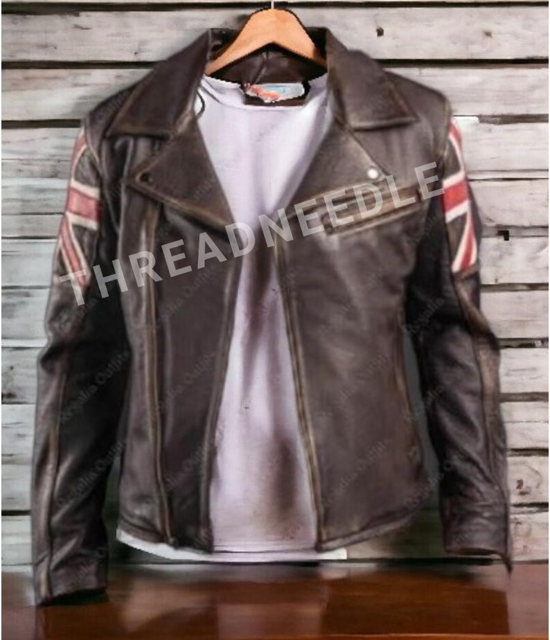 Puede incluir: Chaqueta de cuero marr&oacute;n con un dise&ntilde;o de la bandera de la Union Jack en el hombro derecho. La chaqueta tiene un estilo motero cl&aacute;sico con cuello de solapa y cremallera asim&eacute;trica. Se ve una camiseta blanca debajo.