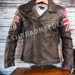Puede incluir: Chaqueta de cuero marr&oacute;n con dise&ntilde;o de la bandera de la Union Jack en las mangas. La chaqueta tiene cierre de cremallera, m&uacute;ltiples bolsillos y un estilo motero cl&aacute;sico. El texto "THREADNEEDLE" es visible.