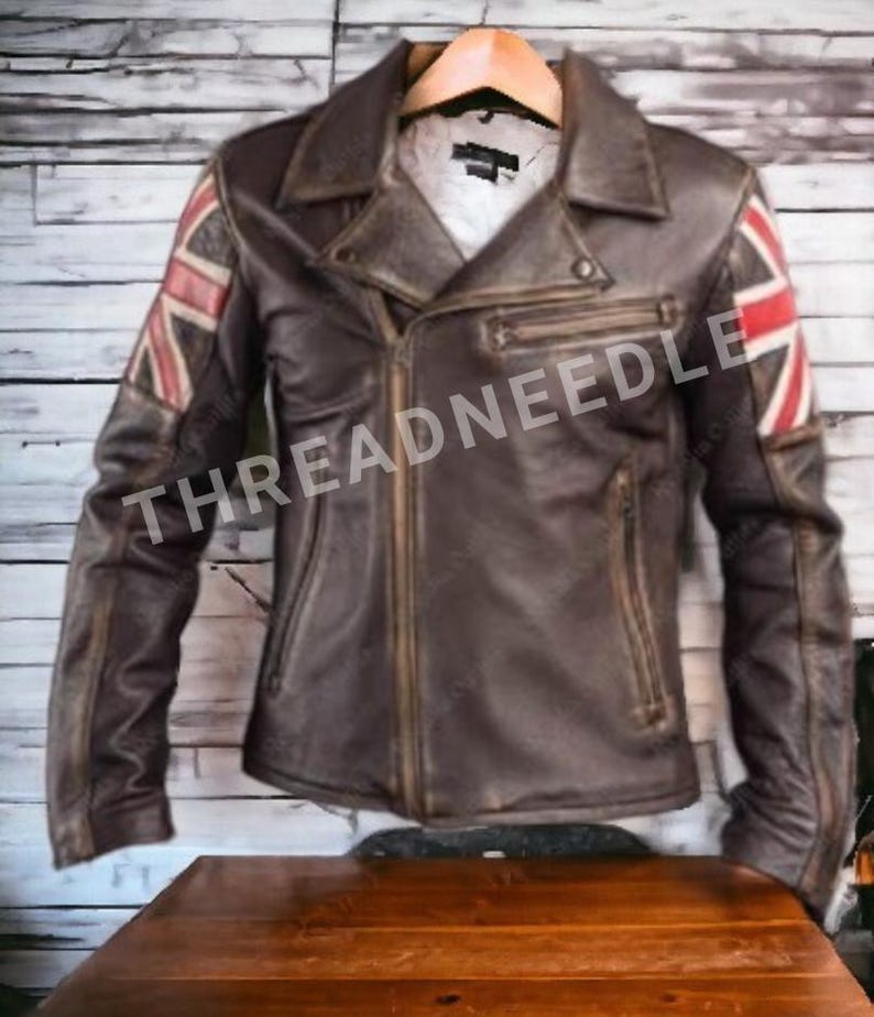 Puede incluir: Chaqueta de cuero marr&oacute;n con dise&ntilde;o de la bandera de la Union Jack en las mangas. La chaqueta tiene cierre de cremallera, m&uacute;ltiples bolsillos y un estilo motero cl&aacute;sico. El texto "THREADNEEDLE" es visible.
