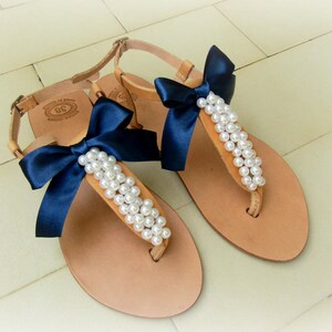 May include: A pair of tan leather sandals with navy blue bows and pearl embellishments.