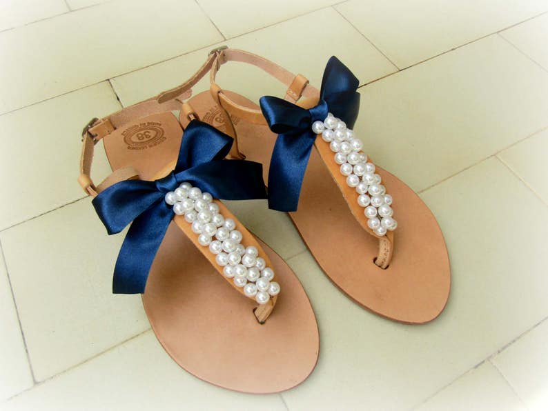 May include: A pair of tan leather sandals with navy blue bows and pearl embellishments.