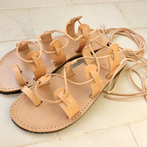 Puede incluir: Un par de sandalias de cuero marr&oacute;n con cordones que se atan en las piernas. Las sandalias tienen un dise&ntilde;o sencillo con m&uacute;ltiples correas y est&aacute;n hechas de cuero suave y flexible.