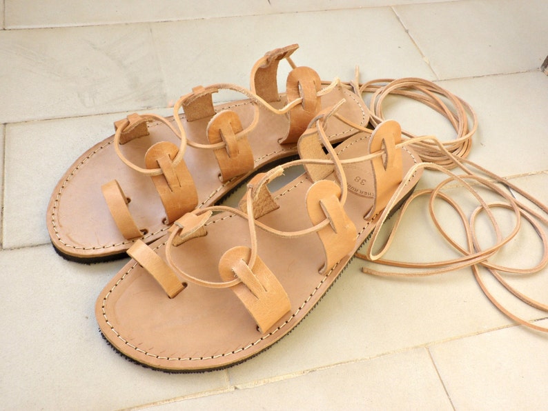 Puede incluir: Un par de sandalias de cuero marr&oacute;n con cordones que se atan en las piernas. Las sandalias tienen un dise&ntilde;o sencillo con m&uacute;ltiples correas y est&aacute;n hechas de cuero suave y flexible.