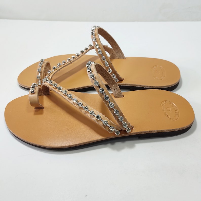 Op de afbeelding: Tan lederen sandalen met een teenring en meerdere banden versierd met heldere strass steentjes.