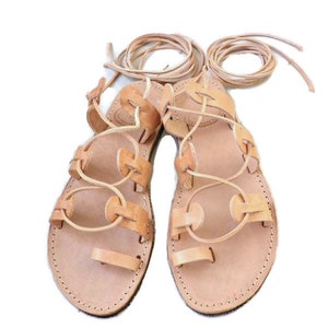 Puede incluir: Un par de sandalias de cuero color canela con cordones que se atan en las piernas. Las sandalias tienen un dise&ntilde;o sencillo con punta redonda y suela plana.