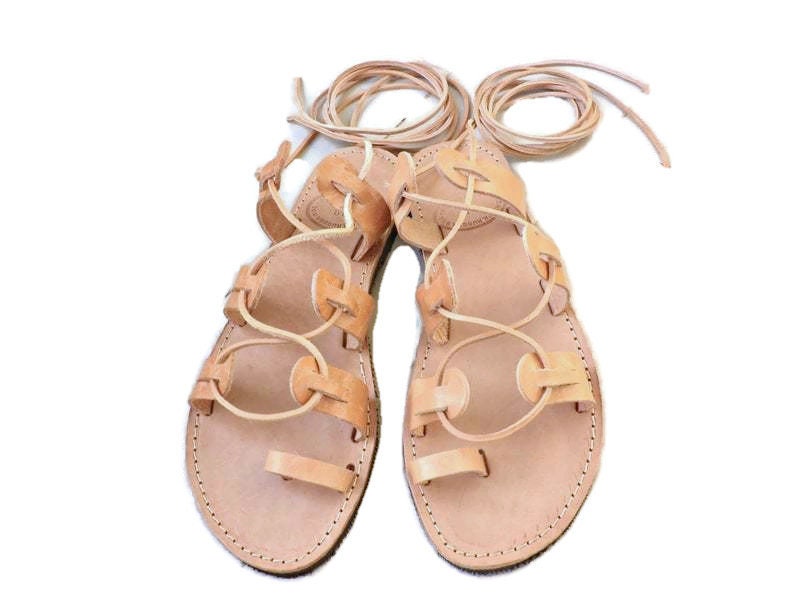 Puede incluir: Un par de sandalias de cuero color canela con cordones que se atan en las piernas. Las sandalias tienen un dise&ntilde;o sencillo con punta redonda y suela plana.