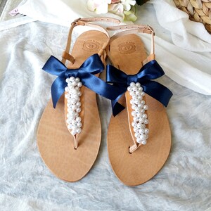 May include: A pair of tan leather sandals with navy blue ribbon bows and pearl embellishments.
