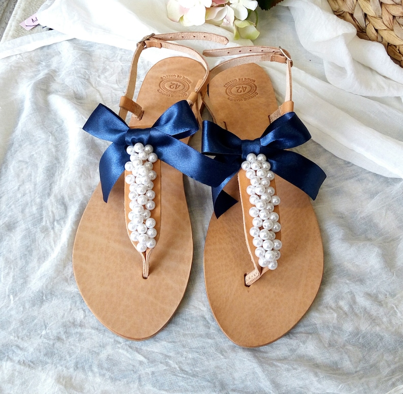 May include: A pair of tan leather sandals with navy blue ribbon bows and pearl embellishments.