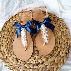 May include: A pair of tan leather sandals with navy blue ribbon bows and pearl embellishments.