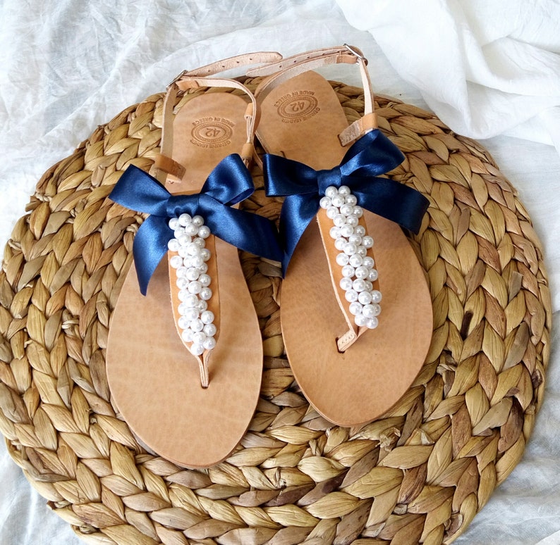 May include: A pair of tan leather sandals with navy blue ribbon bows and pearl embellishments.