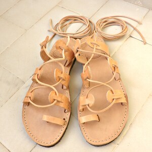 Puede incluir: Un par de sandalias de cuero color canela con cordones que se atan en la pierna. Las sandalias tienen un dise&ntilde;o sencillo con punta redonda y suela plana.