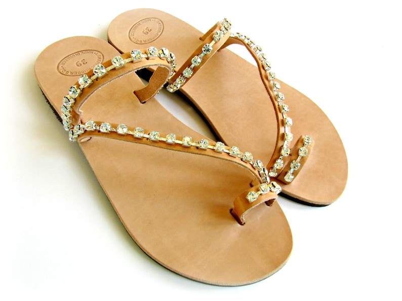 Op de afbeelding: Een paar bruine leren sandalen met een teenring en meerdere banden versierd met heldere strass.