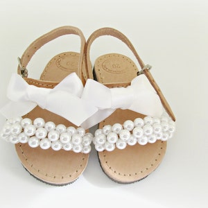May include: White leather sandals with a white satin bow and pearl embellishments.