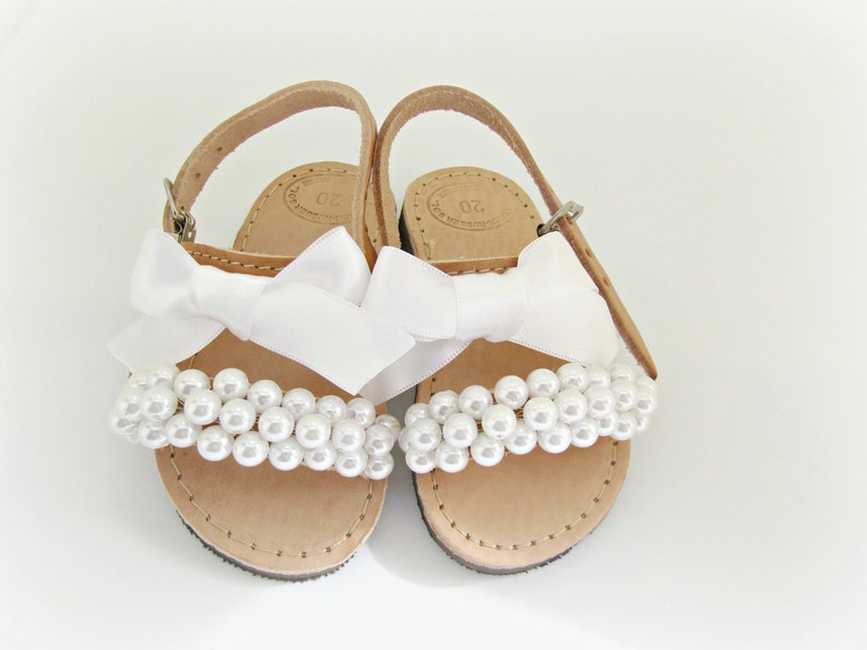 May include: White leather sandals with a white satin bow and pearl embellishments.