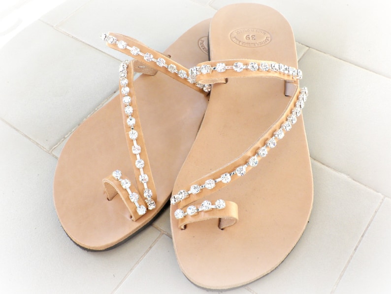 Op de afbeelding: Een paar bruine leren sandalen met een teenriem en meerdere banden versierd met heldere strass.