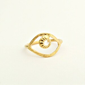 May include: Gold-toned ring with an eye-shaped design. The eye is open and has a detailed, textured iris.