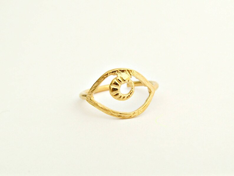 May include: Gold-toned ring with an eye-shaped design. The eye is open and has a detailed, textured iris.