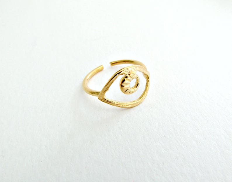 May include: Gold-toned ring with an eye-shaped design. The eye is outlined in a thin metal band and has a textured center.