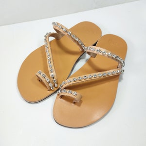 Op de afbeelding: Een paar bruine leren sandalen met meerdere banden versierd met rijen strass.