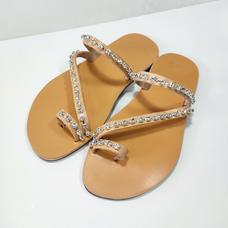 Op de afbeelding: Een paar bruine leren sandalen met meerdere banden versierd met rijen strass.