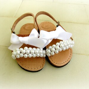 May include: A pair of brown leather sandals with white satin bows and pearl embellishments.