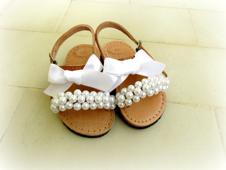 May include: A pair of brown leather sandals with white satin bows and pearl embellishments.