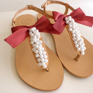 May include: A pair of brown leather sandals with a burgundy ribbon and pearl embellishments.