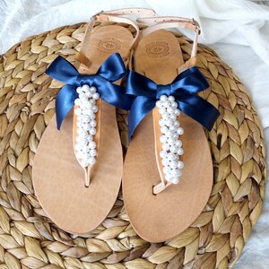 May include: A pair of tan leather sandals with a navy blue ribbon bow and white pearl embellishments.