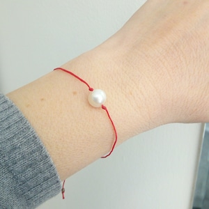 May include: A red string bracelet with a single white pearl charm.