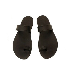 Pode incluir: Um par de sandálias de couro preto com uma tira para o dedo do pé e uma única tira na parte superior do pé.