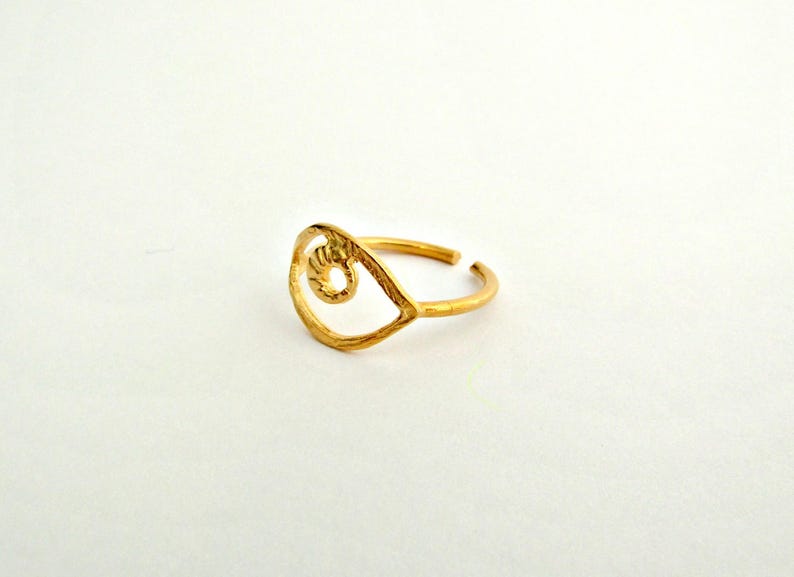 May include: Gold-toned ring with an eye-shaped design. The ring is made of metal and has a simple, minimalist style.