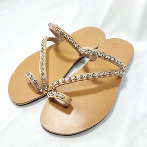 Op de afbeelding: Een paar bruine leren sandalen met meerdere banden versierd met heldere strass.