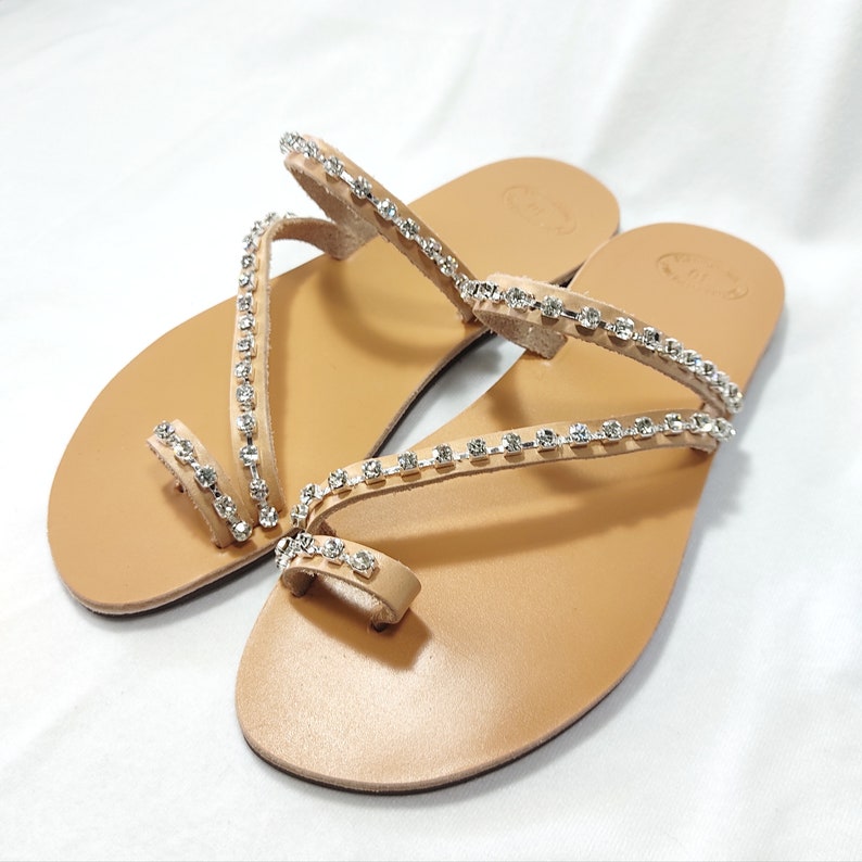 Op de afbeelding: Een paar bruine leren sandalen met meerdere banden versierd met heldere strass.