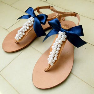 May include: A pair of tan leather sandals with white pearl embellishments and navy blue satin bows.