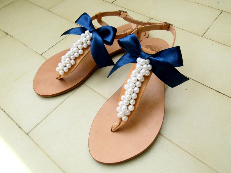May include: A pair of tan leather sandals with white pearl embellishments and navy blue satin bows.