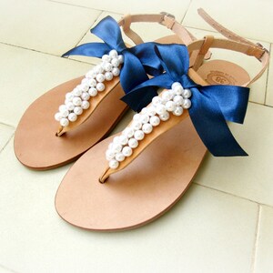 May include: A pair of brown leather sandals with navy blue ribbon bows and pearl embellishments.