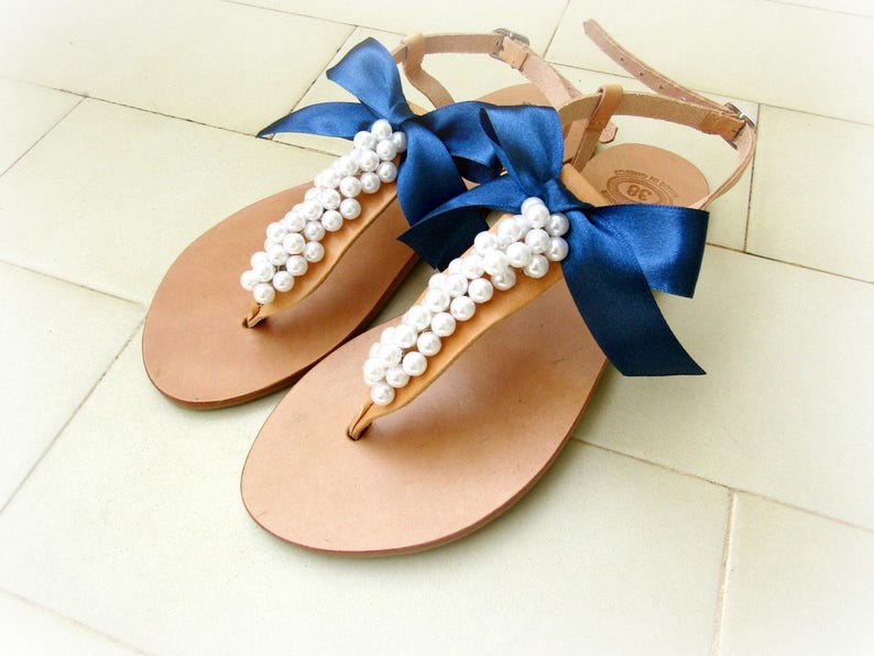 May include: A pair of brown leather sandals with navy blue ribbon bows and pearl embellishments.