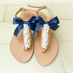 May include: A pair of tan leather sandals with navy blue bows and pearl embellishments.